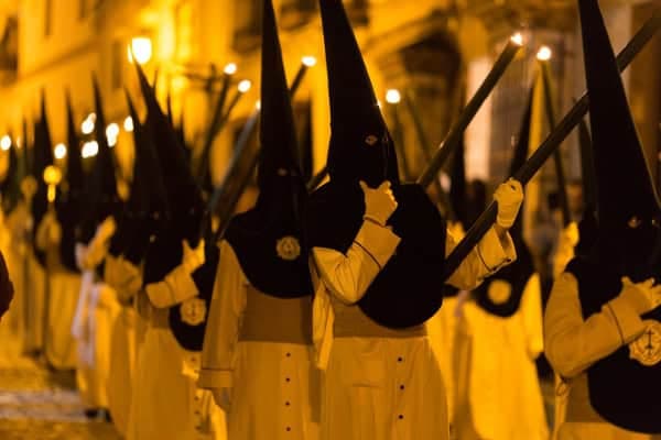 Nazarenos con capirote puntiagudo en una procesión nocturna